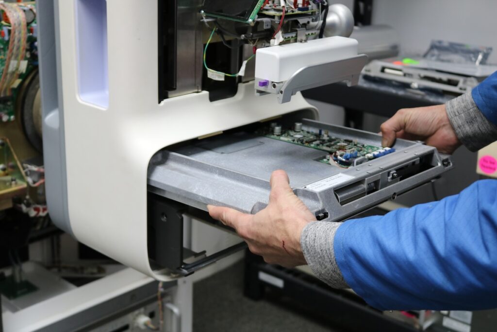 Technician inspecting internal circuit boards during mammography equipment refurbishment