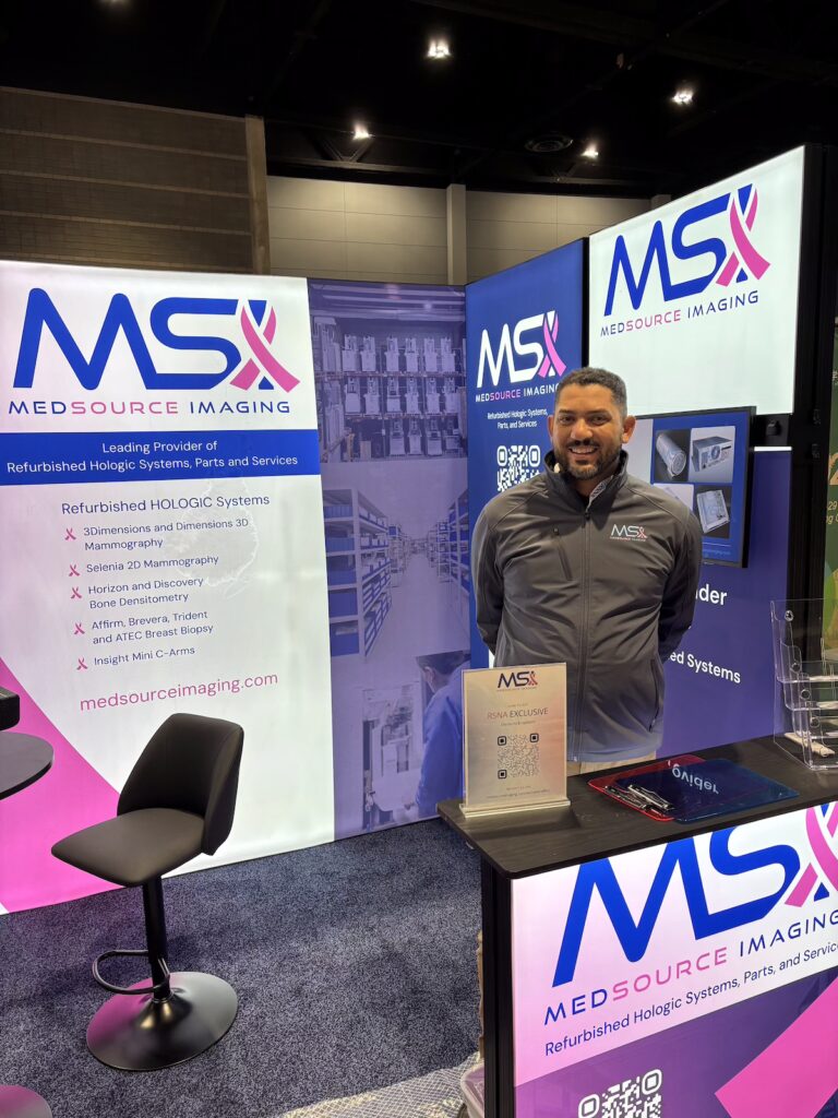 MedSource Imaging team member at the company’s RSNA booth, in front of banners listing refurbished Hologic mammography, bone densitometry, and breast biopsy systems.